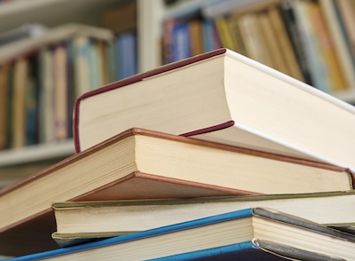 Closed book or textbook on a pile of other books in front of a bookcase in a library. Education learning concept. Image with selective focus.