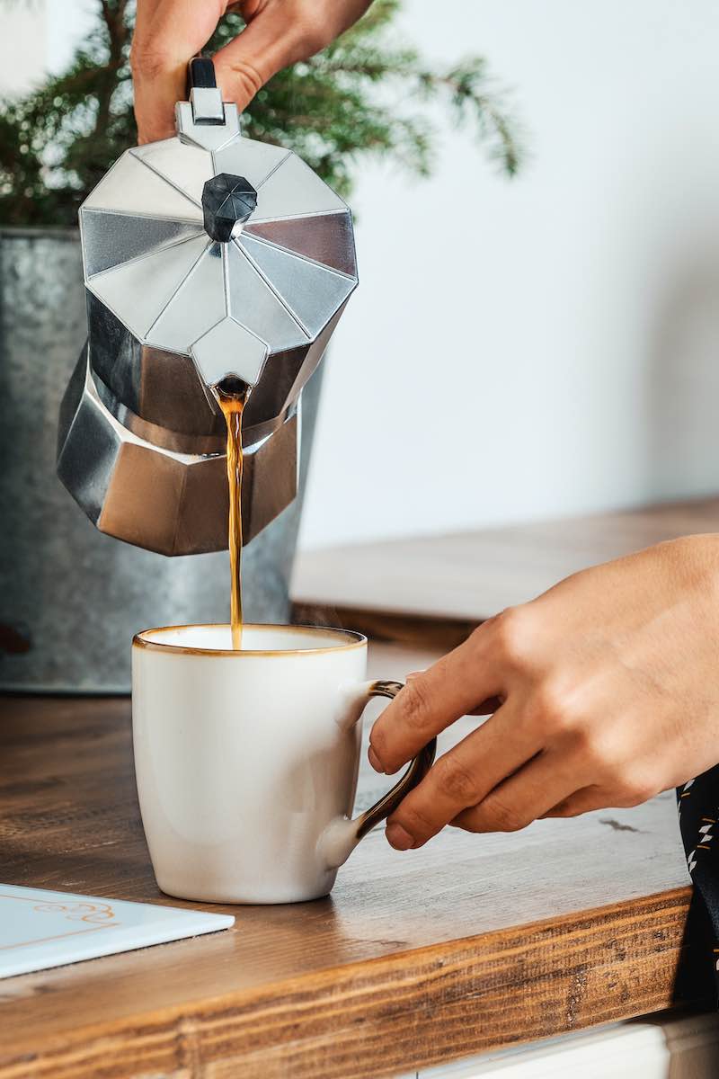 Close up view of female hand pouring coffee from the geyser coffee maker into cup